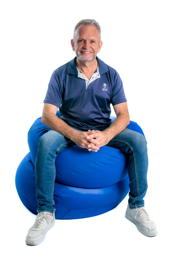 Principal Leon vd Westhuizen, smiling, seated on a blue cushion