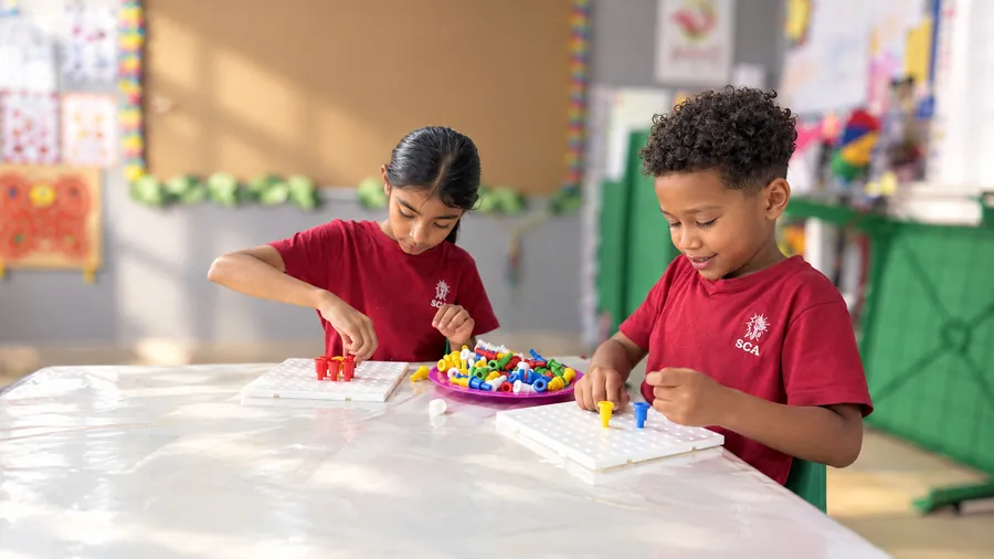 Two young learners concentrating on a colourful pegboard activity in class