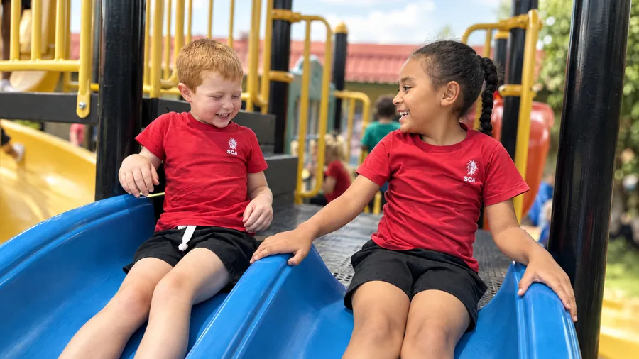 Two Grade RR and R learners laughing together on the playground slide